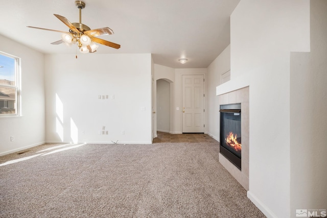 unfurnished living room featuring arched walkways, baseboards, light carpet, and a tiled fireplace