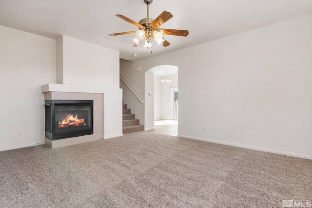 unfurnished living room with arched walkways, carpet flooring, ceiling fan, a tile fireplace, and baseboards