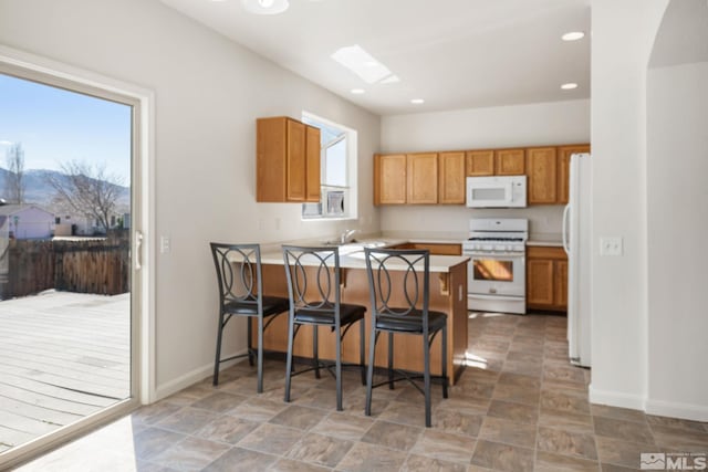 kitchen featuring white appliances, brown cabinetry, a peninsula, light countertops, and a kitchen bar