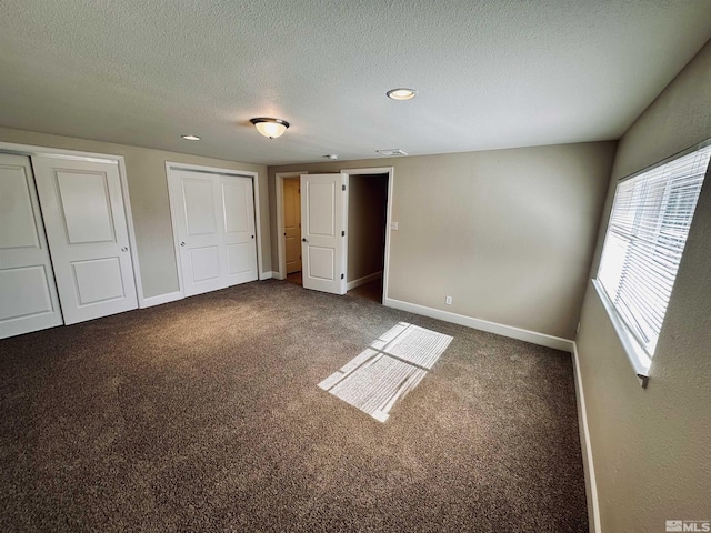 unfurnished bedroom featuring carpet floors, a textured ceiling, baseboards, and multiple closets