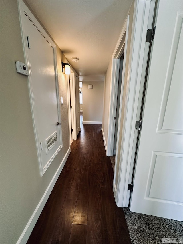 corridor with dark wood-style floors, visible vents, and baseboards