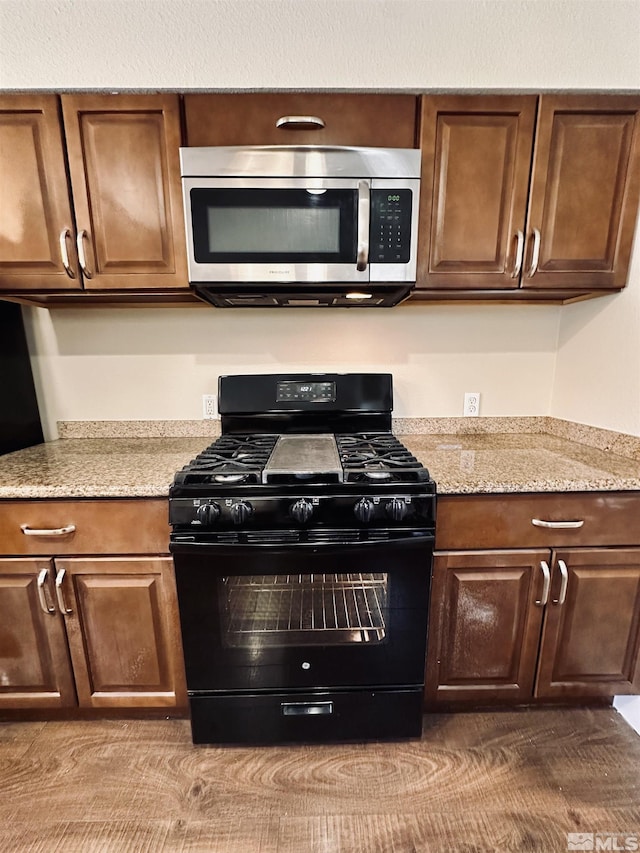 kitchen with black gas stove, light stone countertops, and stainless steel microwave