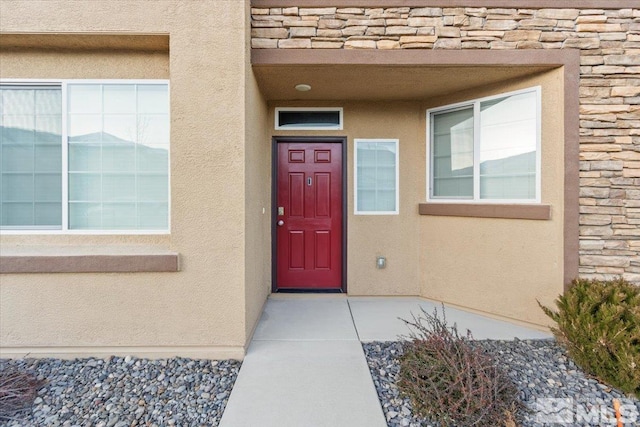 entrance to property with a garage, stone siding, and stucco siding