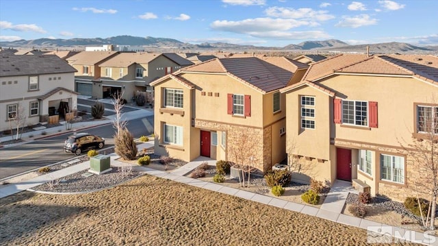 multi unit property with a residential view, stone siding, a mountain view, and stucco siding