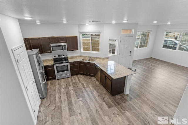 kitchen with dark brown cabinets, appliances with stainless steel finishes, light wood-type flooring, and a sink