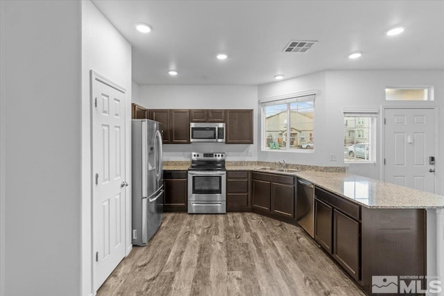 kitchen featuring appliances with stainless steel finishes, light stone counters, a peninsula, light wood-style floors, and a sink