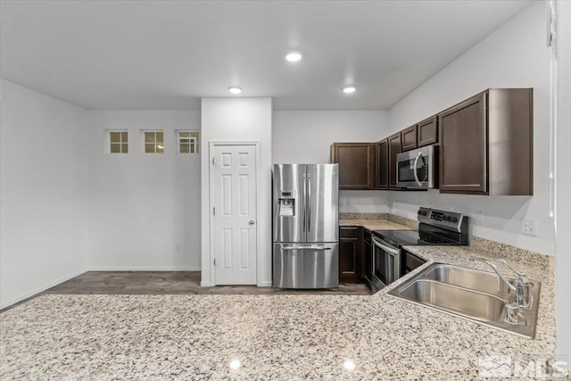 kitchen featuring light stone countertops, appliances with stainless steel finishes, dark brown cabinets, and a sink