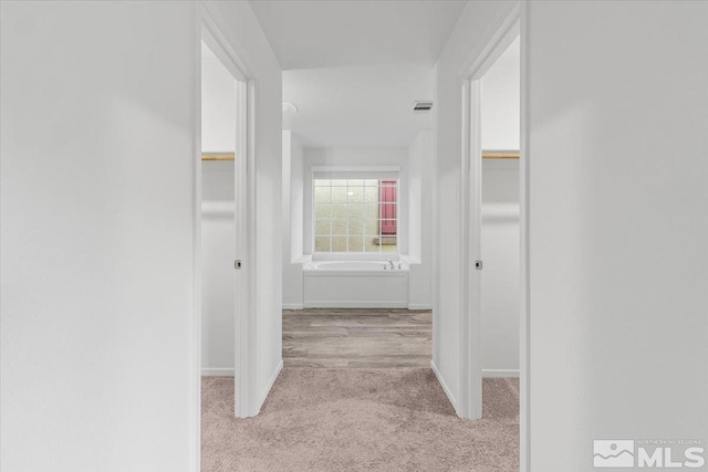 hallway with baseboards, visible vents, and light colored carpet