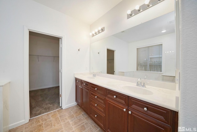 full bathroom featuring a walk in closet, a sink, baseboards, and double vanity