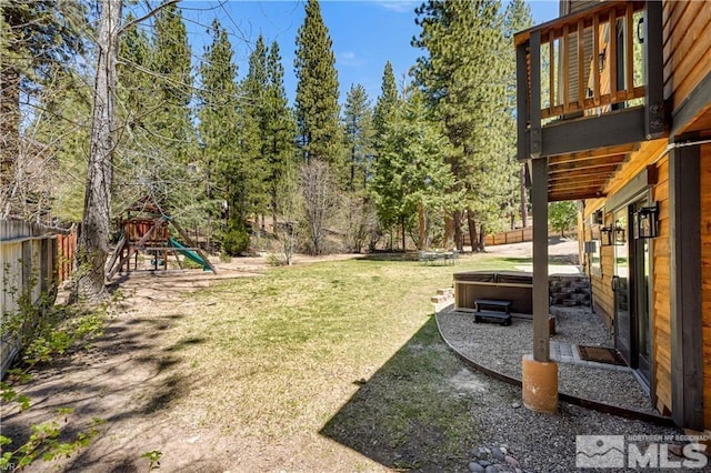 view of yard featuring a fenced backyard, a playground, and a hot tub