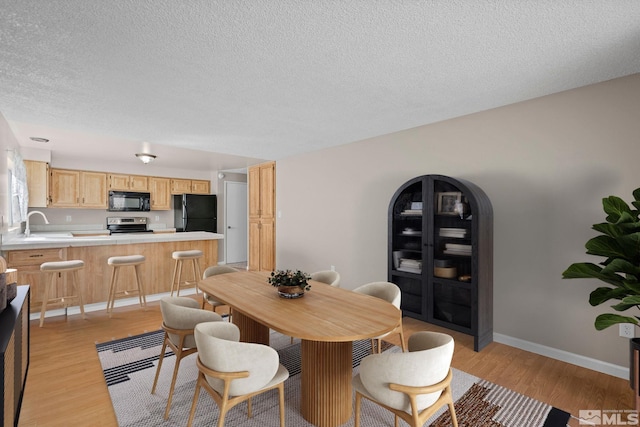 dining room featuring light wood-style floors, baseboards, arched walkways, and a textured ceiling