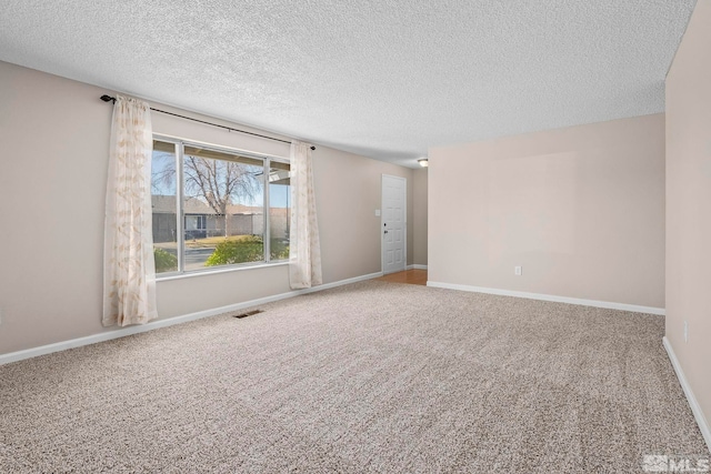 empty room featuring carpet floors, visible vents, a textured ceiling, and baseboards