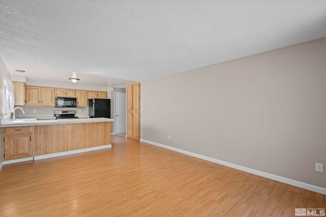 kitchen featuring light wood finished floors, light countertops, light brown cabinets, a peninsula, and black appliances