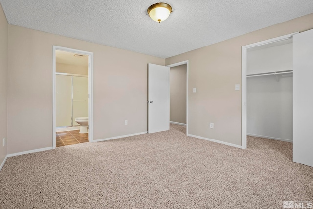 unfurnished bedroom with a textured ceiling, light colored carpet, baseboards, a closet, and a walk in closet