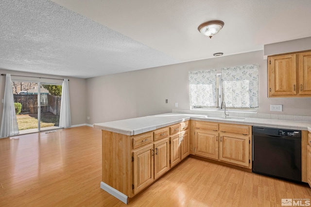 kitchen featuring dishwasher, a peninsula, a sink, and light wood-style flooring