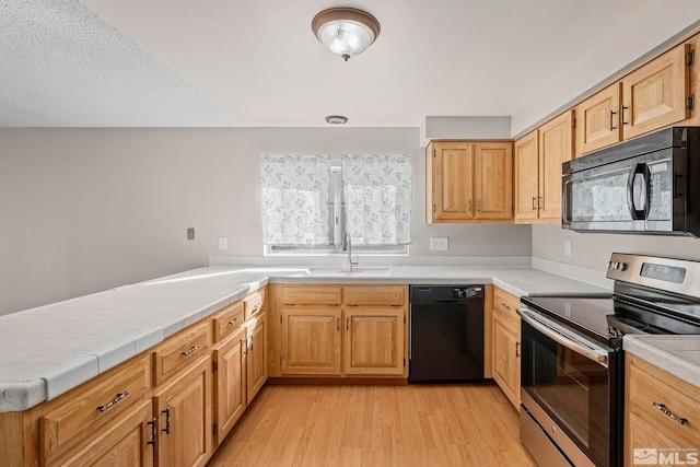 kitchen featuring tile countertops, black appliances, a sink, and light wood-style flooring