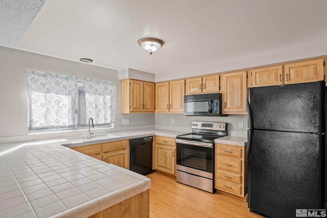 kitchen featuring light wood-style floors, tile countertops, light brown cabinetry, black appliances, and a sink