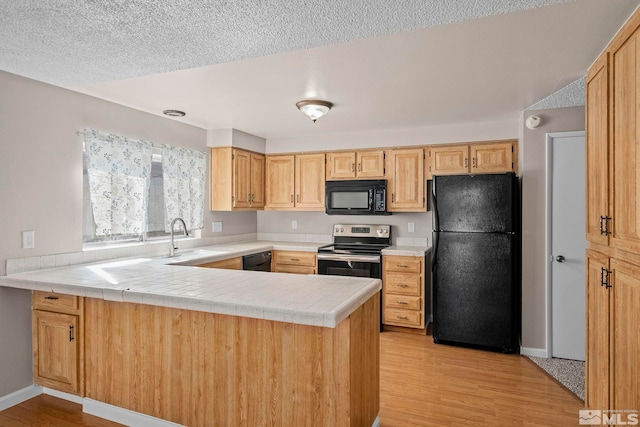 kitchen featuring tile countertops, black appliances, a peninsula, and a sink