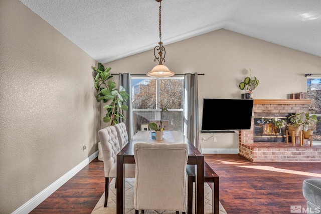 dining room featuring a brick fireplace, vaulted ceiling, baseboards, and wood finished floors