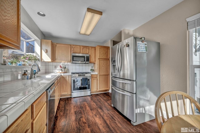 kitchen with decorative backsplash, tile countertops, dark wood-type flooring, stainless steel appliances, and a sink