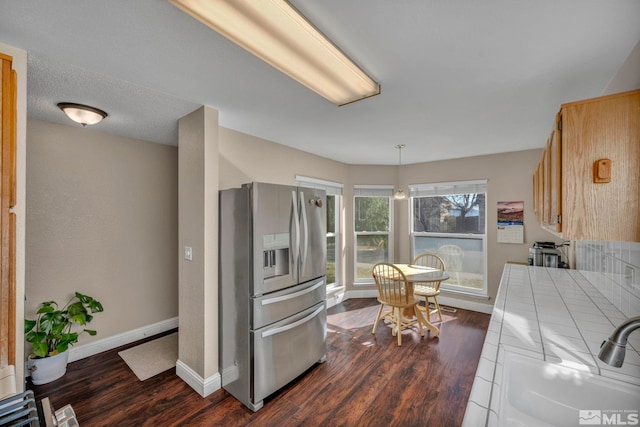 kitchen featuring baseboards, stainless steel fridge with ice dispenser, tile countertops, dark wood-style flooring, and a sink