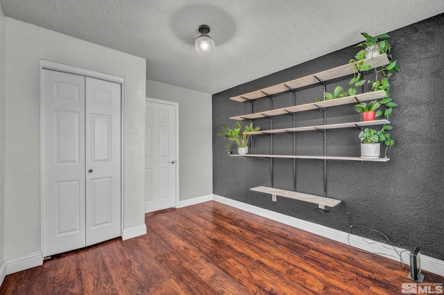 unfurnished bedroom featuring a textured ceiling, baseboards, and wood finished floors