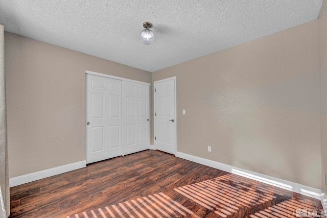 unfurnished bedroom with a textured ceiling, dark wood-style flooring, a closet, and baseboards