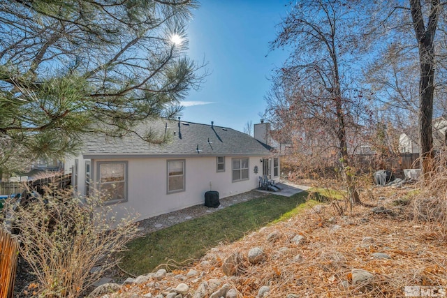 back of property with a shingled roof, a chimney, and fence