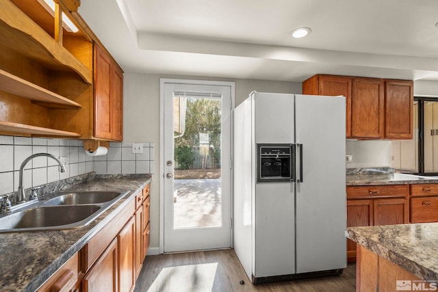 kitchen featuring dark wood-style floors, white fridge with ice dispenser, brown cabinetry, and a sink