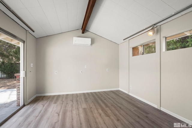 empty room featuring light wood-style floors, a wall unit AC, vaulted ceiling with beams, and baseboards