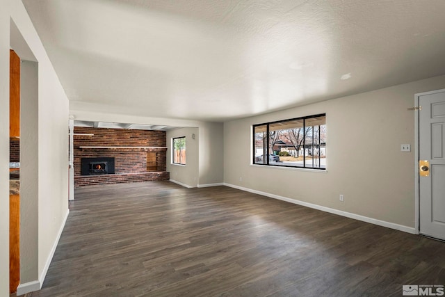 unfurnished living room with dark wood-style flooring, a brick fireplace, a wealth of natural light, and baseboards