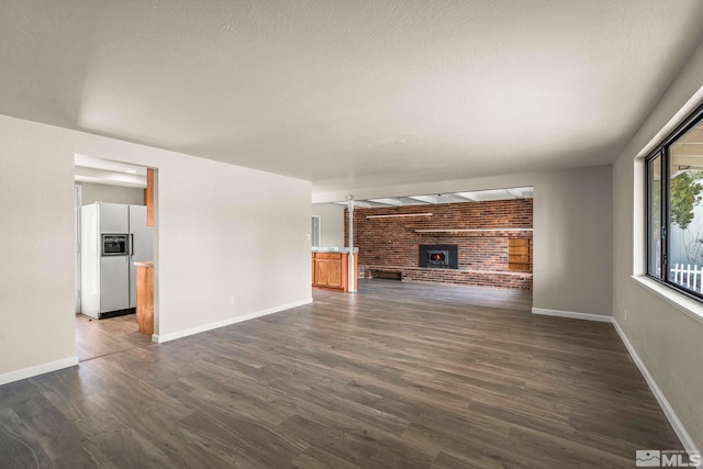 unfurnished living room with a brick fireplace, dark wood finished floors, and baseboards