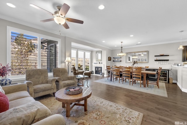 living area featuring recessed lighting, ornamental molding, a glass covered fireplace, wood finished floors, and baseboards