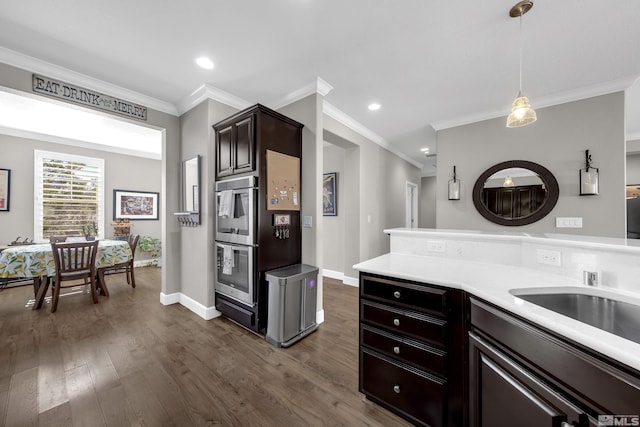 kitchen featuring baseboards, dark wood-style floors, ornamental molding, light countertops, and pendant lighting