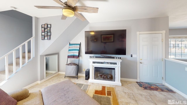 living area with stairway, a glass covered fireplace, and baseboards