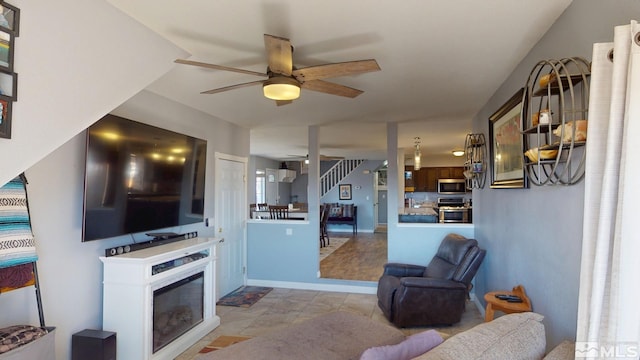 living area featuring a ceiling fan, a glass covered fireplace, and baseboards