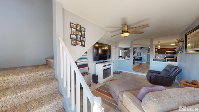 living area with a ceiling fan, a fireplace, and stairs