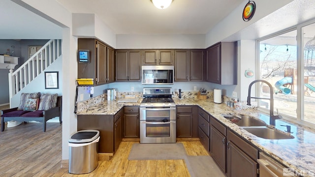 kitchen featuring light stone countertops, light wood finished floors, stainless steel appliances, and a sink