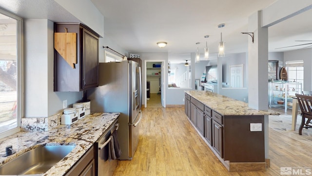 kitchen with ceiling fan, dark brown cabinetry, a center island, light wood-type flooring, and light stone countertops