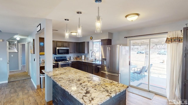 kitchen with light stone counters, decorative light fixtures, light wood finished floors, appliances with stainless steel finishes, and a sink