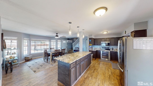 kitchen featuring pendant lighting, appliances with stainless steel finishes, dark brown cabinetry, a kitchen island, and light wood-type flooring