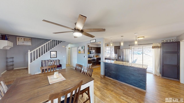 dining room with stairs, light wood-type flooring, a ceiling fan, and baseboards