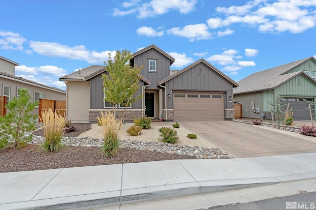 view of front of home featuring a garage, stone siding, fence, decorative driveway, and board and batten siding