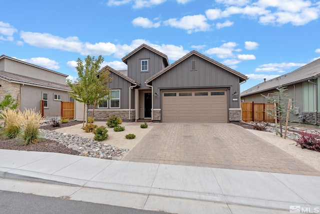 craftsman inspired home with decorative driveway, an attached garage, board and batten siding, fence, and stone siding