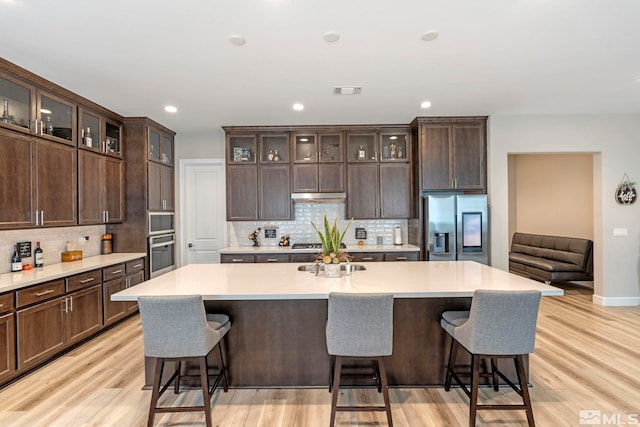 kitchen featuring an island with sink, light wood-style flooring, stainless steel appliances, and light countertops