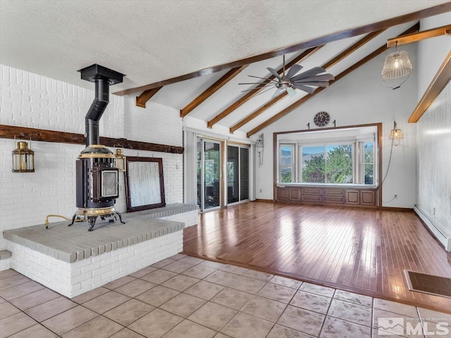 unfurnished living room featuring baseboard heating, a wood stove, a textured ceiling, and beam ceiling