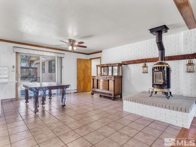 living area featuring a ceiling fan, brick wall, a wood stove, a textured ceiling, and light tile patterned flooring