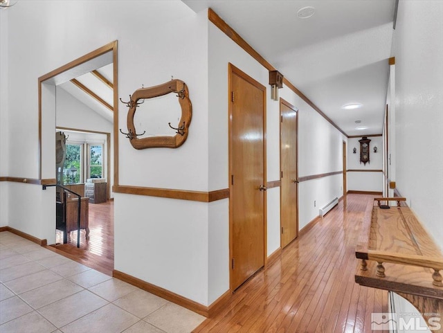 hall featuring lofted ceiling, light wood-style flooring, baseboards, baseboard heating, and crown molding