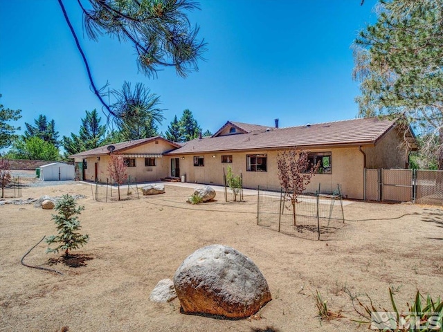 back of property with an outbuilding, a gate, a storage unit, fence, and stucco siding