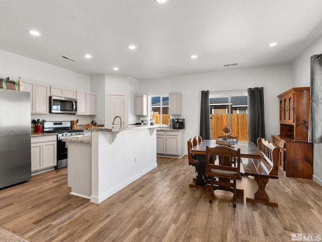 kitchen featuring appliances with stainless steel finishes, a center island with sink, light wood-style flooring, and a kitchen bar